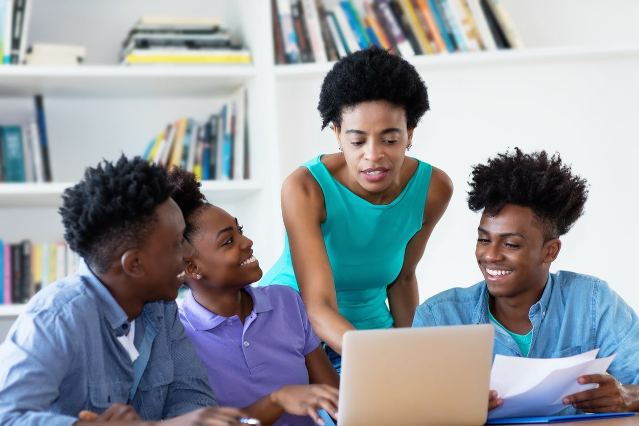 Female teacher and her three students looking at a laptop