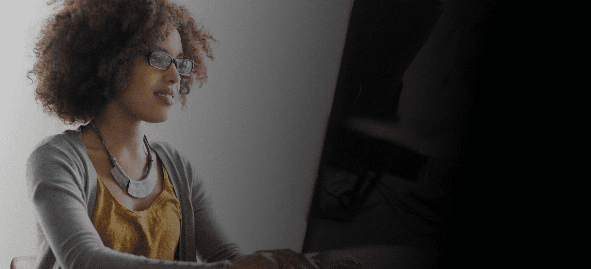 Woman with curly hair and glasses working on a computer.