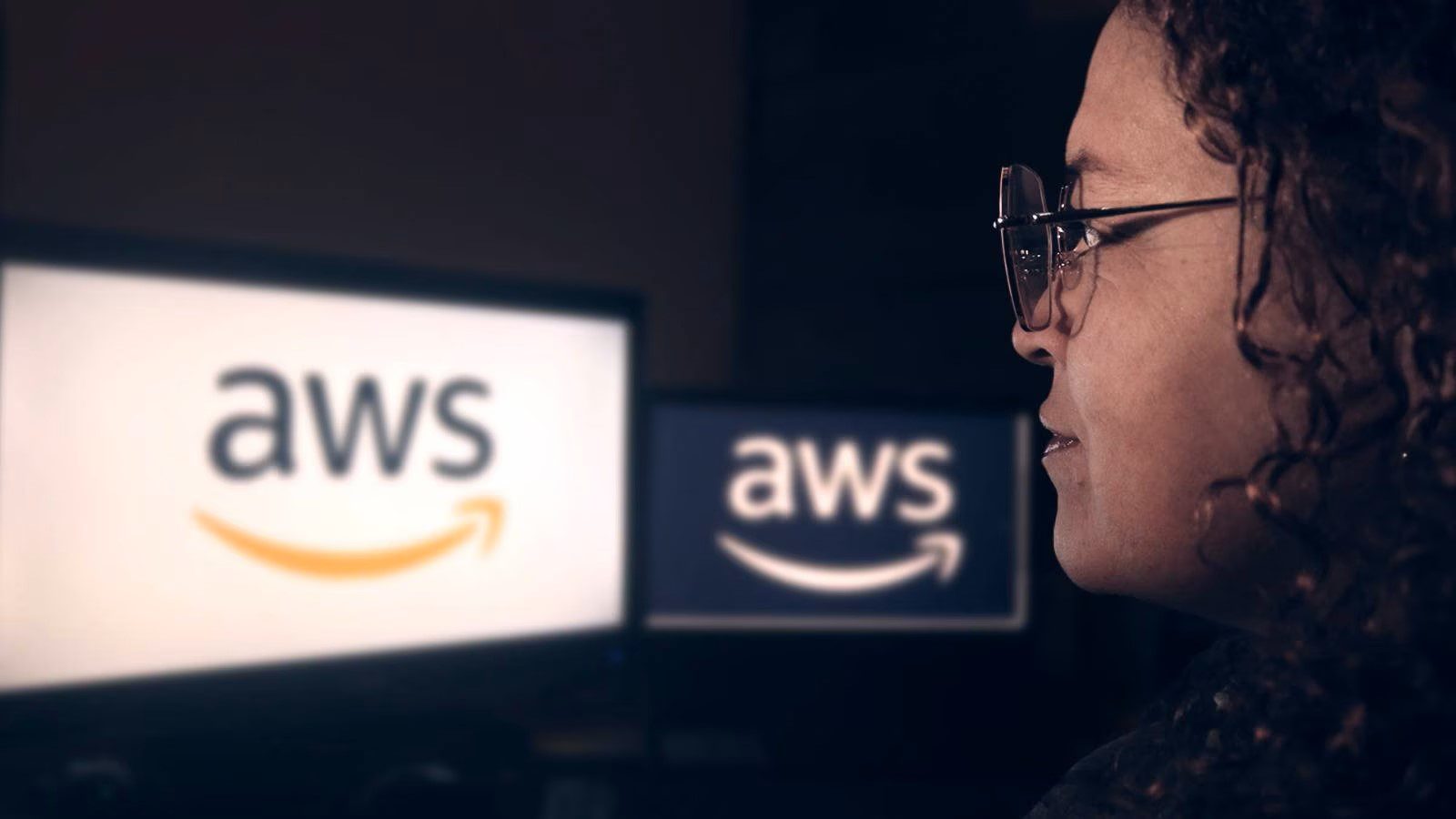 A woman wearing glasses gazes at an AWS logo displayed on a computer screen