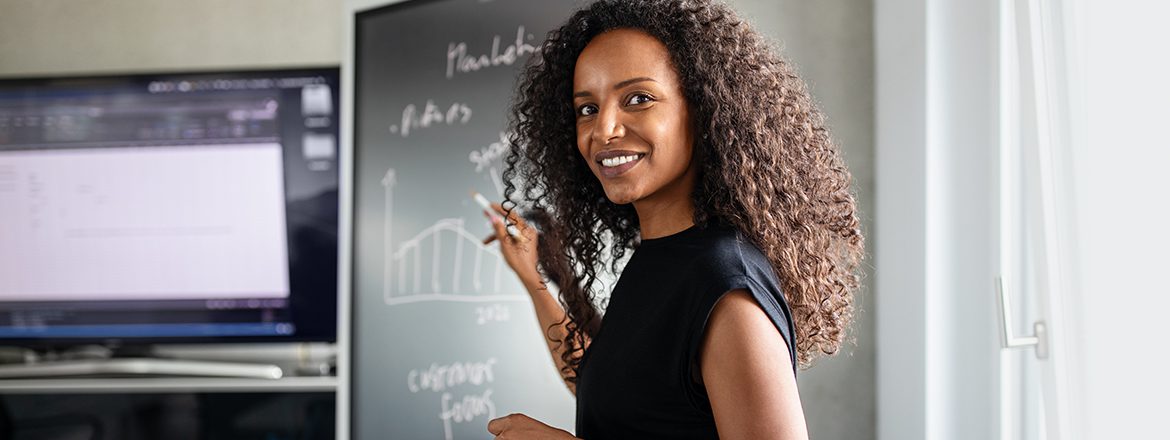 Featured image for article titled "Why Digital Upskilling is a Key Component in Business Transformation" showing a woman presenting a chart on a blackboard.