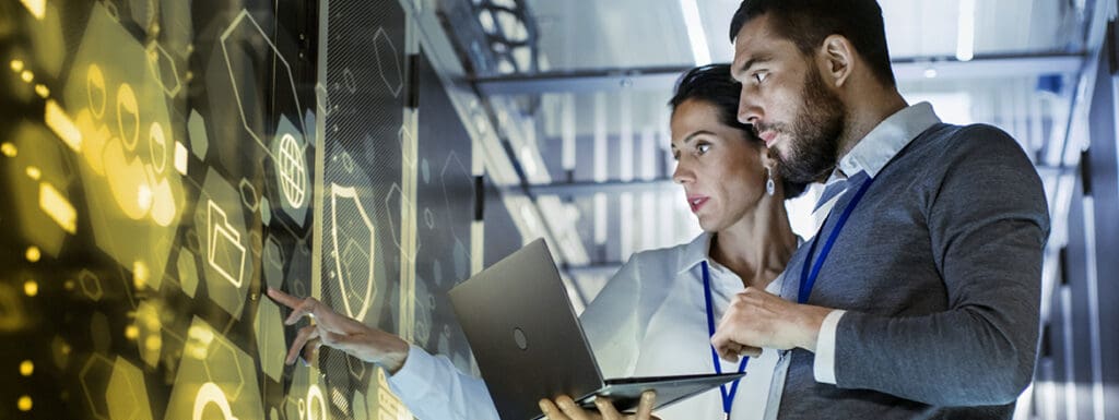 Featured image for article titled "Strategies to Overcome the AI Skills Gap in Your Organization" showing two people looking at a computer in a server room.